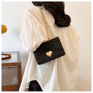 Detail of black quilted chain bag with a gold heart-shaped metal twist lock closure