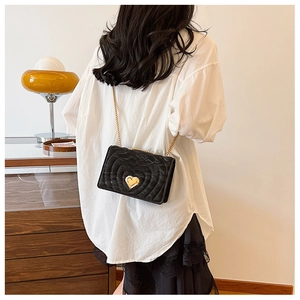 Detail of black quilted heart-lock crossbody bag with gold chain shown on a model