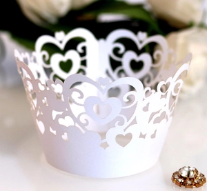 Laser cut white paper cupcake wrappers with intricate heart patterns for wedding decor