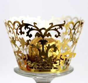 Elegant gold laser-cut cupcake wrapper with floral vine lace pattern on glass stand