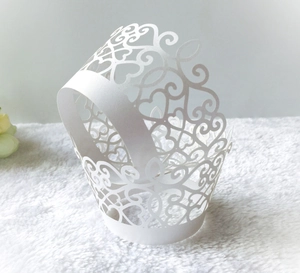White laser-cut filigree cupcake wrappers with heart lace pattern on plush background