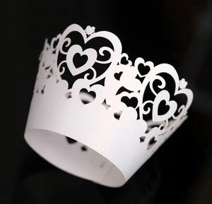 Detailed laser-cut heart lace pattern on a white paper cupcake wrapper over black background