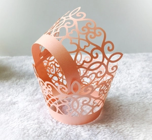 Laser cut light orange lace cupcake wrappers with heart and vine patterns on plush background