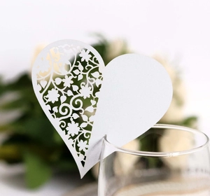 Close-up of laser-cut white heart place card with floral hollow pattern on wine glass