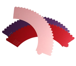 Detail of laser-cut cupcake wrappers in pink and red with wavy edges and tab closures