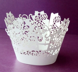 Close-up of white laser-cut cupcake wrappers with rose flower and lace vine patterns