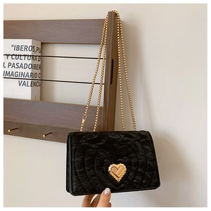 Detail of black quilted velvet crossbody bag with golden heart lock and chain strap
