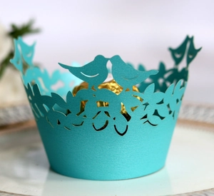 Close-up of cyan laser-cut cupcake wrapper with bird and floral filigree pattern