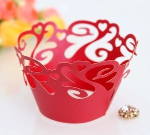 Macro shot of laser-cut red cupcake wrappers with heart scroll patterns and glossy finish