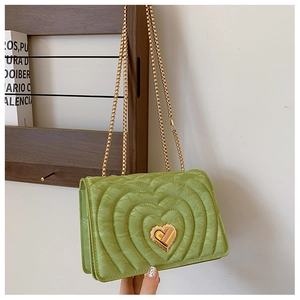Detail showing heart quilted texture and golden heart-shaped twist lock on green chain bag