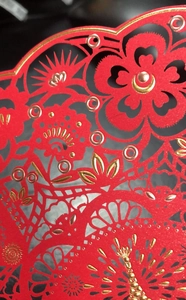 Macro shot of laser-cut red paper card with intricate gold foil floral patterns