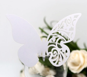 Close-up of white laser-cut butterfly place card with floral hollow pattern on a glass