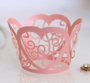 Detail of pink laser-cut cupcake wrapper with hollow heart and floral vine patterns
