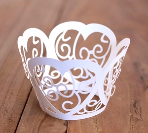 Detail of laser-cut heart pattern and vine scrolls on white cupcake wrappers