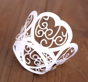 Macro shot of white laser-cut cupcake wrappers with heart lace pattern on wood