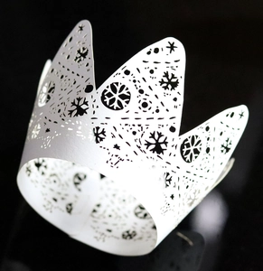 Laser-cut white crown cupcake wrapper featuring intricate snowflake patterns on black background