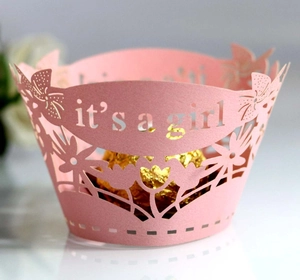 Macro detail of pink laser-cut cupcake wrapper with It's a Girl text and floral patterns