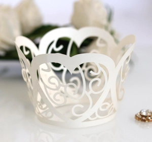 Macro shot of white laser-cut cupcake wrapper featuring intricate heart vine patterns