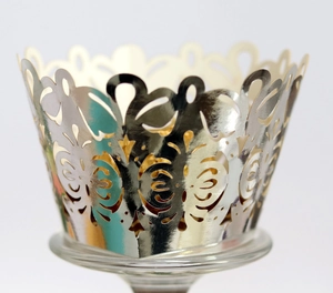 Macro shot of silver laser-cut cupcake wrapper with floral vine pattern on glass tray