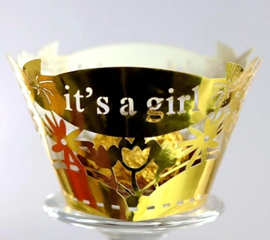 Macro shot of gold laser-cut cupcake wrapper with it's a girl text and floral pattern