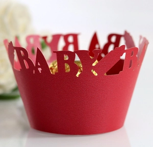 Detail view of red laser-cut paper cupcake wrapper featuring hollow BABY text design