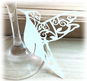 White laser-cut hummingbird place card with spiral patterns for wine glass decoration