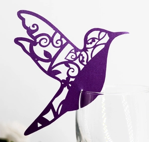 Laser-cut dark purple hummingbird place card on wine glass with elegant filigree pattern