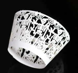 Macro detail of laser-cut Halloween cupcake wrapper with white spider web and skull motifs