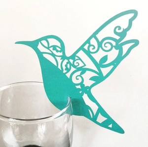 Detail of laser-cut hummingbird paper card in teal blue on a wine glass rim
