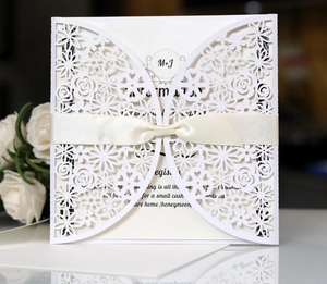 Close-up of laser-cut floral wedding invitation with cream ribbon and pearl paper texture