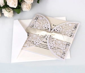 Detail of laser-cut floral wedding invitation with cream sleeve and white ribbon bow