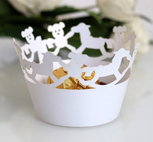 Detail of white laser-cut cupcake wrapper featuring cute bear and rocking horse patterns