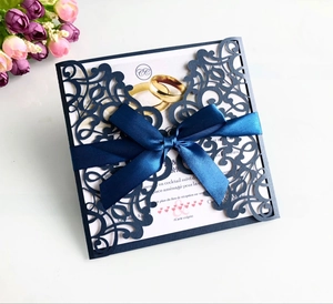 Detail of laser-cut navy wedding invitation with satin ribbon and floral decoration
