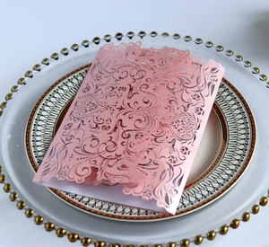 Detailed macro view of laser-cut pearl pink wedding invitation with ornate scroll patterns