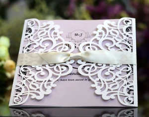 Detail of laser-cut wedding invitation with white floral sleeve and ivory silk bow