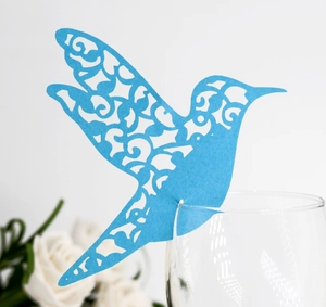 Blue laser-cut hummingbird place card on a wine glass with intricate hollow patterns