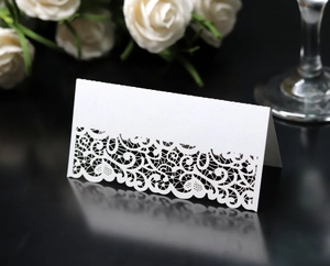 Detail of white laser-cut lace table card with intricate hollow pattern for weddings