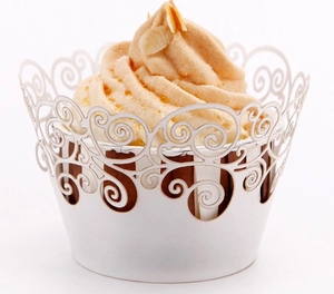 Close-up of white laser-cut cupcake wrappers with elegant vine patterns for wedding decor