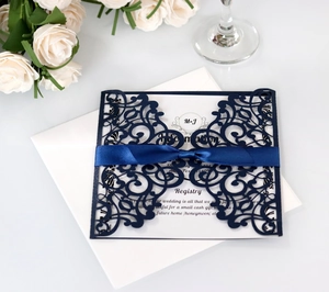 Close-up of laser-cut navy blue wedding invitation with silk ribbon and white envelope