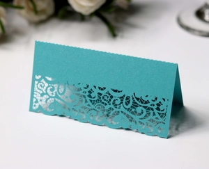Macro detail of laser-cut lace floral pattern on teal pearlized table place cards