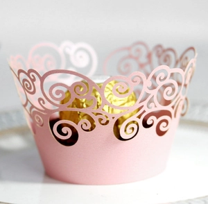 Detail view of pink laser-cut cupcake wrapper with elegant scroll patterns for parties