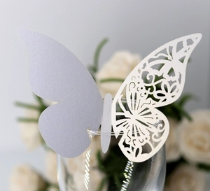 Close-up of laser-cut hollow butterfly paper card on a glass rim for wedding decor