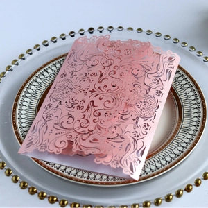 Pink laser-cut lace invitation card with elegant floral patterns on a vintage ceramic plate