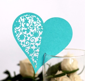 Teal laser-cut heart place card with floral patterns on a glass rim for weddings