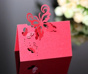 Macro shot of laser-cut red glitter wedding place card featuring elegant butterfly designs