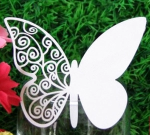 Laser-cut white butterfly place card with intricate scrollwork on a wine glass rim