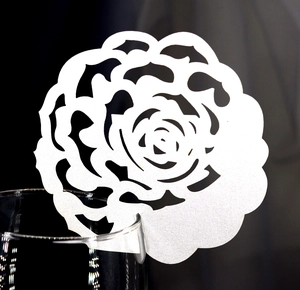 Detailed laser-cut white rose paper card delicately hanging on a glass rim for weddings