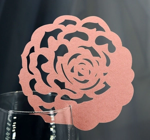 Detail of pink laser-cut rose paper place card attached to the rim of a glass