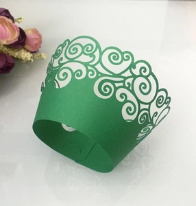 Close-up of laser-cut green cupcake wrapper with intricate scroll patterns on a white surface