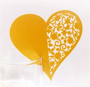 Golden heart-shaped place card with laser-cut floral patterns on a glass rim